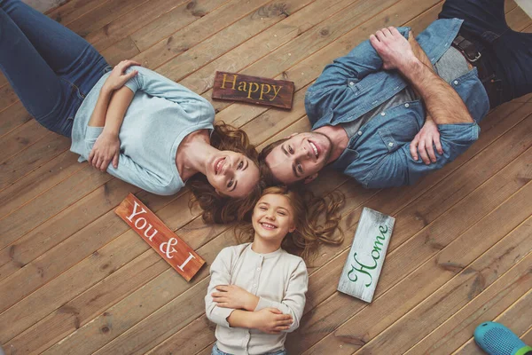 美丽的年轻家庭在相机和微笑 而躺在木地板在家里的顶视图 三块木板躺在家附近 — 图库照片