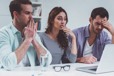 İki genç çekici işadamları ve gündelik giysiler içinde bir güzel iş kadını dizüstü bilgisayar kullanarak ve ofiste çalışırken üzgün olmak