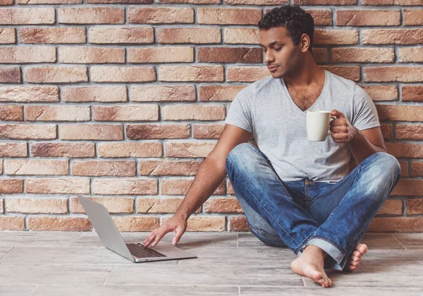 Młody Przystojny Afro Amerykański Mężczyzna Dżinsach Korzystający Laptopa Trzymający Kubek — Zdjęcie stockowe