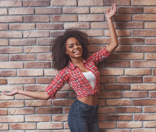 若いです美しいですアフリカ系アメリカ人女性ポーズと笑顔しながらレンガの壁に立って — ストック写真
