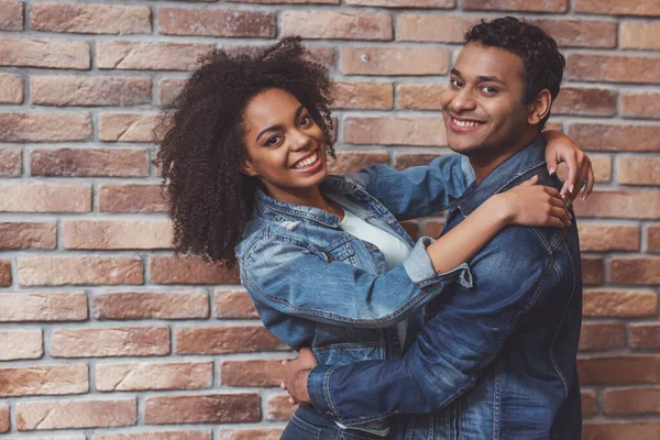 若い魅力的なアフリカ系アメリカ人のカップルの抱擁 カメラを見て レンガの壁に対して立って笑顔 — ストック写真