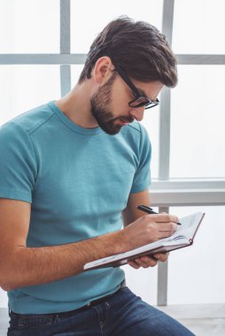 Yakışıklı adam rahat kıyafetler ve notlar pencere yanında otururken not defterinde yapma gözlük