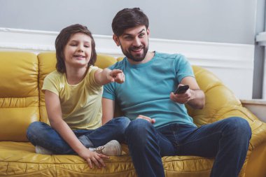 Yakışıklı genç Baba rahat kıyafetler ve odada bir kanepede otururken bir Tv izlerken şirin küçük oğlu. İşaret ederek, babası bir uzaktan kumanda tutan küçük bir çocuk