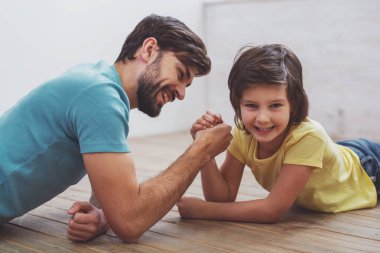 Yakışıklı genç Baba rahat kıyafetler ve bilek güreşi odasında bir ahşap zemin üzerinde yalan sırasında rekabet sevimli küçük oğlu