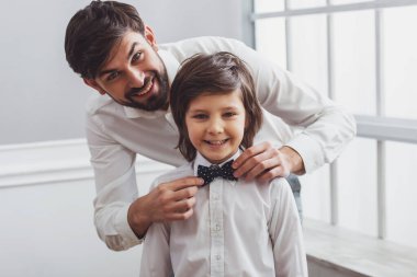 Yakışıklı genç Baba, şirin küçük oğlunun papyon ayarlama. Hem kamera seyir ve gülümseyen klasik gömlek beyaz