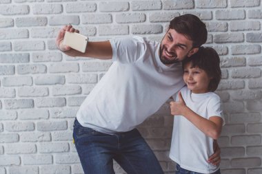Yakışıklı genç Baba şirin küçük oğlu ile bir fotoğraf yapmak. Ok işaret gösteren bir çocuk. İkimiz de gülümseyerek, beyaz duvara karşı ayakta beyaz t-shirt.