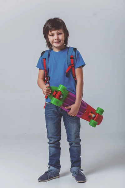 Roztomilý Malý Školák Modré Tričko Batohem Držení Skateboardu Hledá Kameře — Stock fotografie