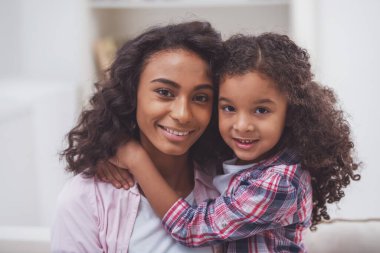 Portre sevimli küçük Afro-Amerikan kız ve onun güzel genç anne sarılma, kamera seyir ve gülümseyen.