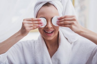 Kafasındaki sünger gözleriyle kapsayan ve gülümseyen bir havlu ile bornoz güzel genç kadın portresi.