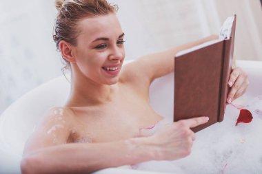Köpük ile keyifli banyo keyfi, bir kitap okuma ve gülümseyen güzel sarışın genç kadın