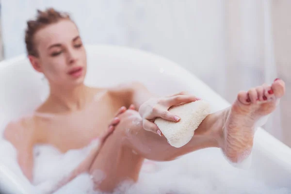 年轻漂亮的女人享受愉快沐浴着泡沫 洗她的腿一缕麻 重点放在腿上 — 图库照片