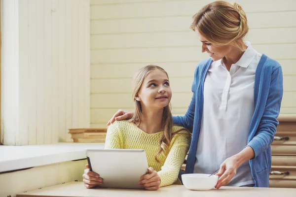 可爱的少女使用的平板电脑 美丽的母亲抱着一大碗 看着对方和微笑着坐在家里 — 图库照片