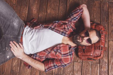 Ahşap bir arka plan üzerinde yatan şık adam rahat gömlek ve kameraya, seyir güneş gözlüğü sakallı Üstten Görünüm