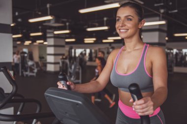 Eliptik bir eğitmen spor salonunda egzersiz ve gülümseyen çekici genç kadın