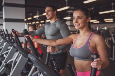Eliptik bir eğitmen spor salonunda egzersiz ve gülümseyen çekici genç insanlar