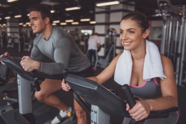 Spor salonunda bir egzersiz bisikleti üzerinde çalışma dışarı ve gülümseyen çekici genç insanlar