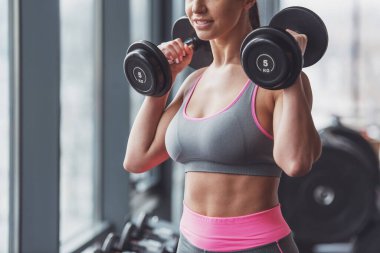 Çekici genç kadın spor salonu ve gülümseyerek dumbbells ile çalışma dışarı yakın çekim