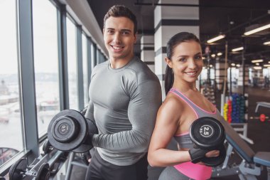 Spor salonunda dumbbells ile çalışma dışarı ve gülümseyerek kameraya bakarak çekici kas gençler