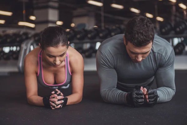 有吸引力的年轻肌肉男人和女人做木板行使在健身房锻炼的时候 — 图库照片
