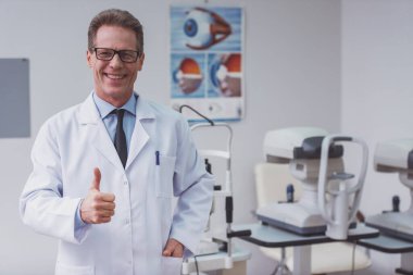 Ok işaret gösteren ve ofisinde dururken gülümseyen yakışıklı orta yaşlı göz doktoru