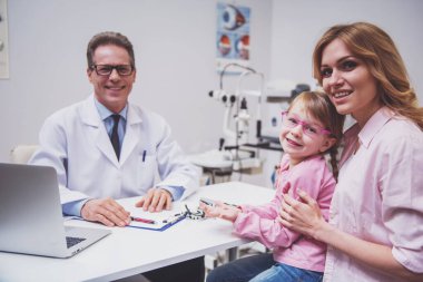 Tatlı küçük kız ve annesi göz doktoruna istişare tarih itibariyle. Tüm kameraya bakıyor ve gülümsüyor