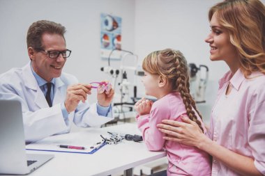 Tatlı küçük kız ve annesi, istişare, gözlük, tüm gülümseyen tutan doktor üzerinde göz doktoru