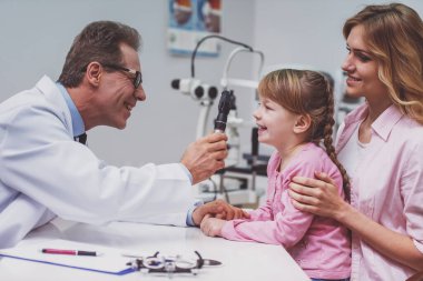 Tatlı küçük kız ve annesi, göz doktoru, Doktor muayene modern ekipman, tüm gülümseyen kızla