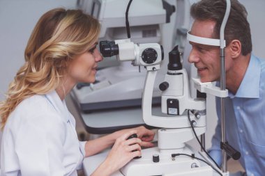 Genç güzel kadın doktoruna yakışıklı orta inceleyerek modern ekipman, her iki gülümseyen adam yaşlı