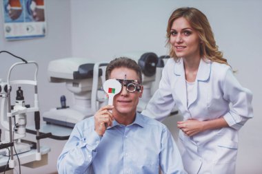 Kapsayan bir göz ve görme keskinliği kontrol göz doktoruna istişare üzerinde yakışıklı orta yaşlı adam. Genç güzel kadın doktor gülümseyen