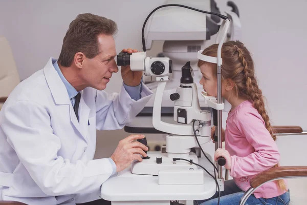 侧面图的英俊眼科医生检查与现代设备的小女孩的眼睛 — 图库照片
