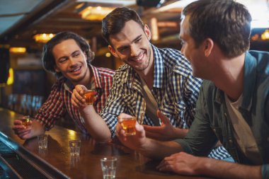 Rahat kıyafetler içinde üç genç adam konuşuyor, gülüyor ve sayaç pub bar, otururken içme