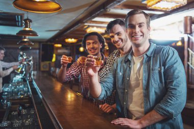 Rahat kıyafetler içinde üç genç adam konuşuyor, gülüyor ve sayaç pub bar, otururken alkollü içecek gözlük tutan