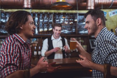 İki erkek rahat kıyafetler, konuşmak ve, counter pub, bar arka planda bir barmen otururken bira içmek