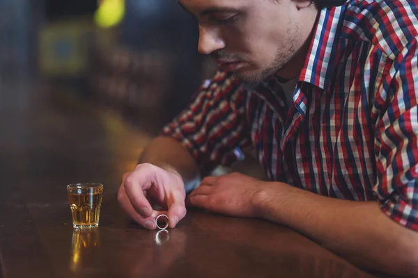 カジュアルな服で悲しい男は バーのパブでカウンターに座ってアルコール飲料のガラスの近く結婚指輪を保持しているクローズ アップ — ストック写真