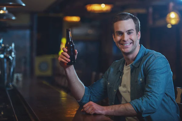 Молода Приваблива Людина Повсякденному Одязі Посміхається Тримає Пляшку Пива Сидячи — стокове фото