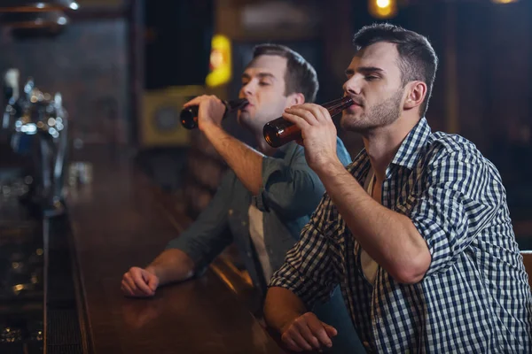 カジュアルな服で 人の若者は バーのパブでカウンターに座ってビールを飲んでいます — ストック写真