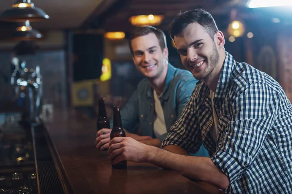 Dos Jóvenes Con Ropa Casual Sonríen Mirando Cámara Sosteniendo Botellas —  Fotos de Stock