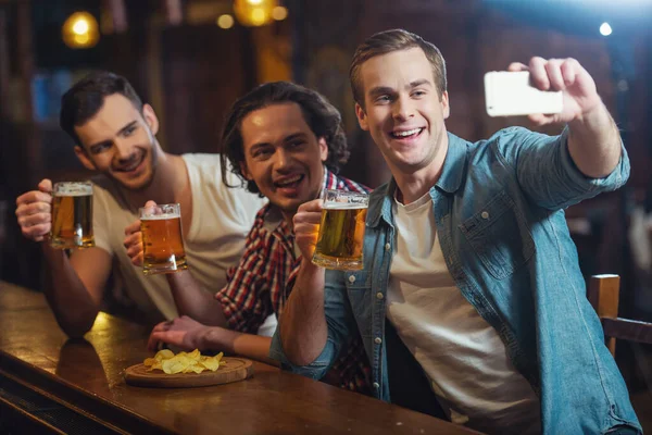 三名年轻男子穿着休闲服微笑 采取自拍照 坐在酒吧柜台在酒吧里喝啤酒 — 图库照片