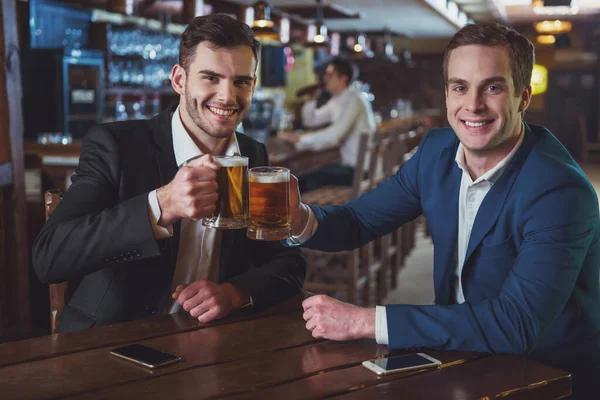 Two Young Businessmen Suits Smiling Looking Camera Clanging Glasses Beer — Stock Photo, Image