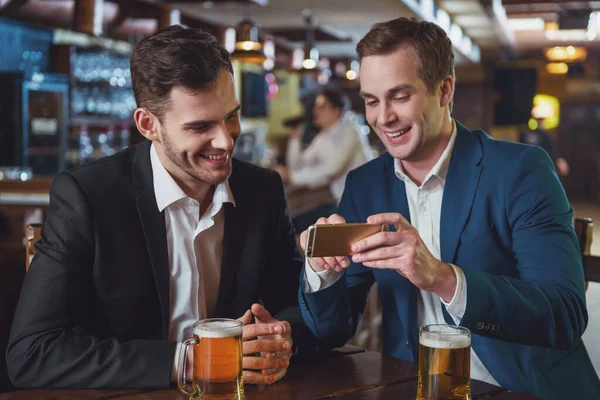 スーツ姿の 人の若いビジネスマンが笑みを浮かべて 携帯電話を使用して パブに座ってビールを飲んで — ストック写真