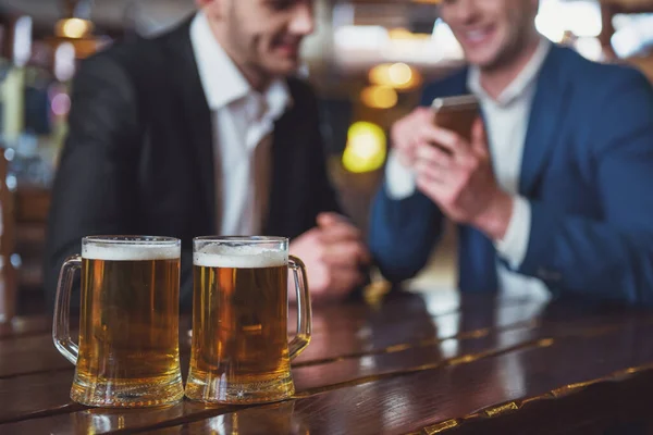 Двое Молодых Бизнесменов Костюмах Улыбаются Пользуются Мобильным Телефоном Пьют Пиво — стоковое фото