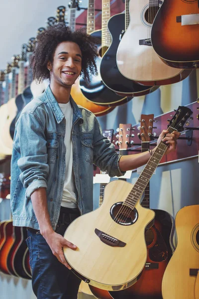 ジーンズ ジャケット ギターを抱えて カメラ目線 音楽店に立ちながら笑顔でハンサムなアフリカ系アメリカ人男性 — ストック写真