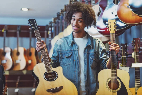 両手で 本のギターを押し 音楽店に立ちながら笑みを浮かべてハンサムな若いアフリカ系アメリカ人男 — ストック写真