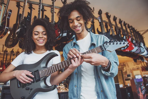 音楽店で美しい若いアフリカ系アメリカ人カップルが立っていたエレク トリック ギターを演奏し 和音を手伝った男ながら笑顔の女の子 — ストック写真
