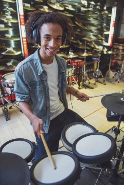 Afro-Amerikan yakışıklı genç gülümseyen bir müzik dükkanında elektronik davul çalarken kot ceketli