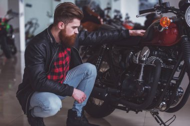 Siyah deri ceketli yakışıklı genç sakallı adamı onun motosiklet inceleyerek