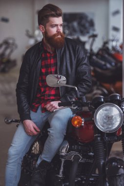 Siyah deri ceketli yakışıklı genç sakallı adamı uzak motosiklet üzerinde otururken arıyor