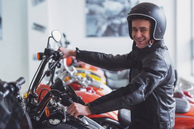 Çekici genç sarışın yan görünüm siyah deri ceketli adam ve kameraya bakarak ve bir motosiklet üzerinde otururken gülümseyen kask