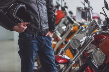 Siyah deri ceketli adamı tutan bir kask ve bir motosiklet salonda motosiklet inceleyerek yakın çekim