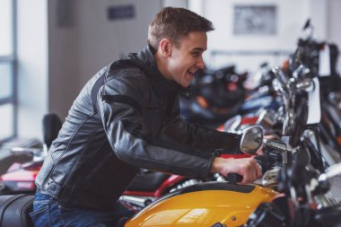 Yan görünümü çekici sarışın gencin binmek taklit ve bir motosiklet üzerinde otururken gülümseyen siyah deri ceket